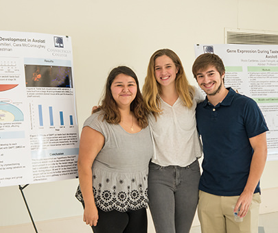 Students pose in front of their presentation board at a conference.