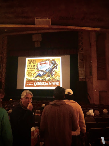 Inside The Garde Theater on stage is projected a poster from a Godzilla remake
