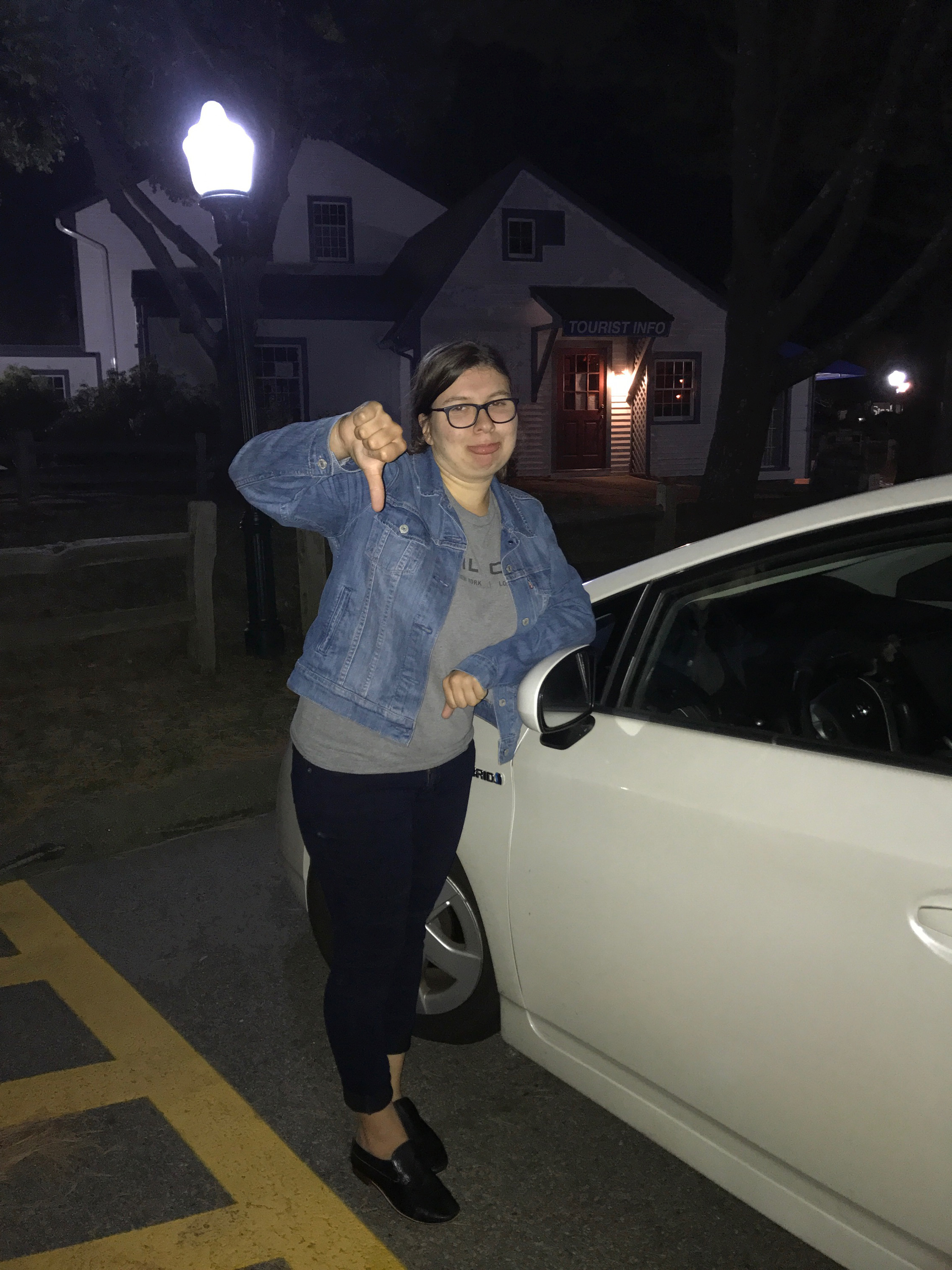 Julia poses with the thumbs down in front of a white compact car