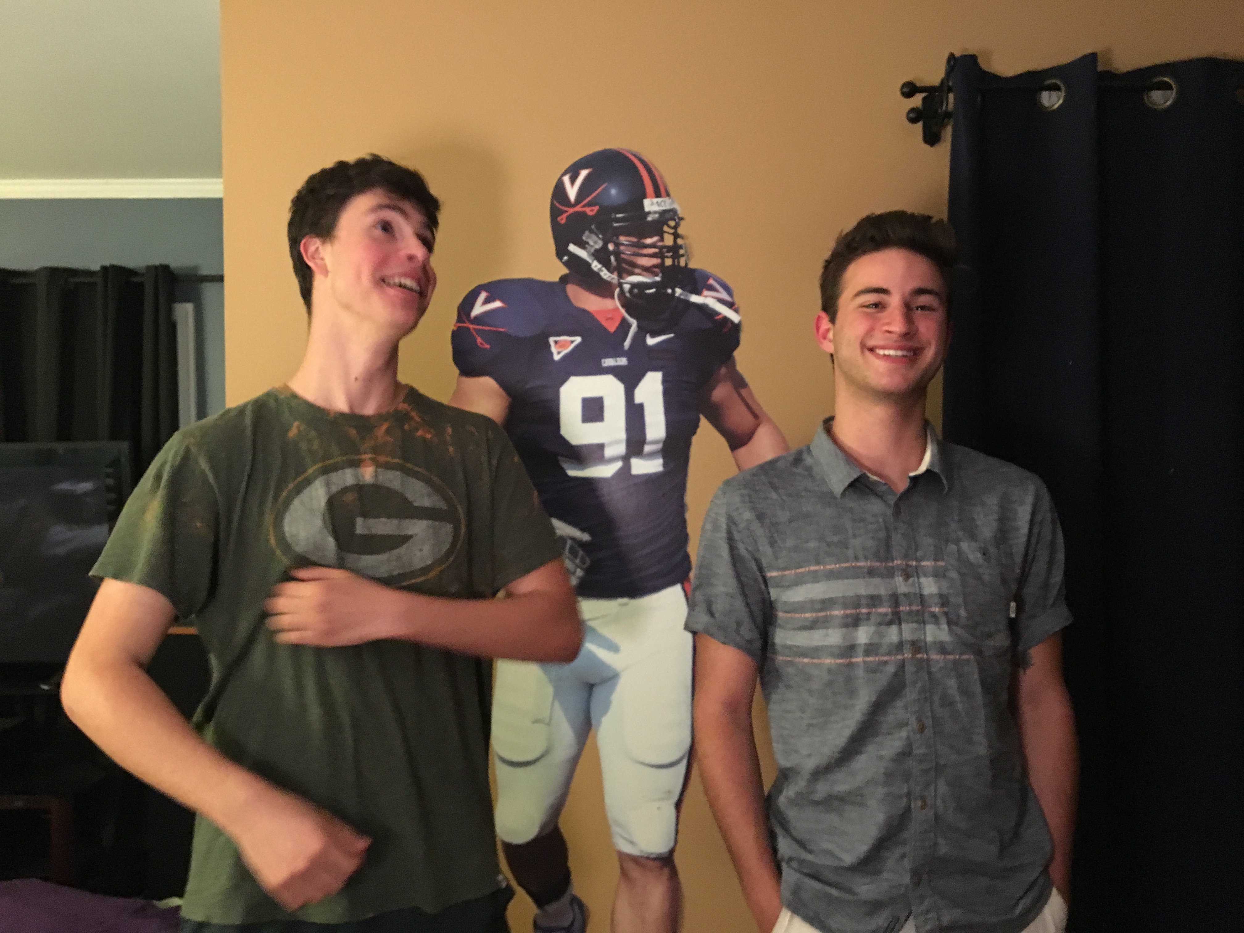 Mark and Samuel pose in front of a stick on wall graphic of a University of Virginia football player