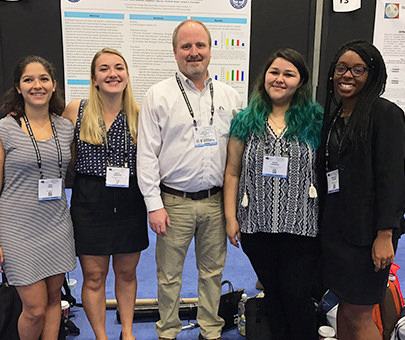 Psychology students and professor Joseph Schroeder pose in front of their presentation board.