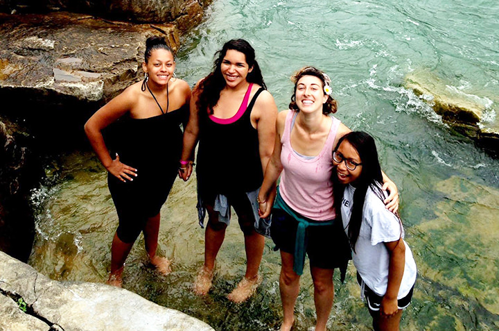 Four sociology students stand in crystal clear water on a trip abroad. 