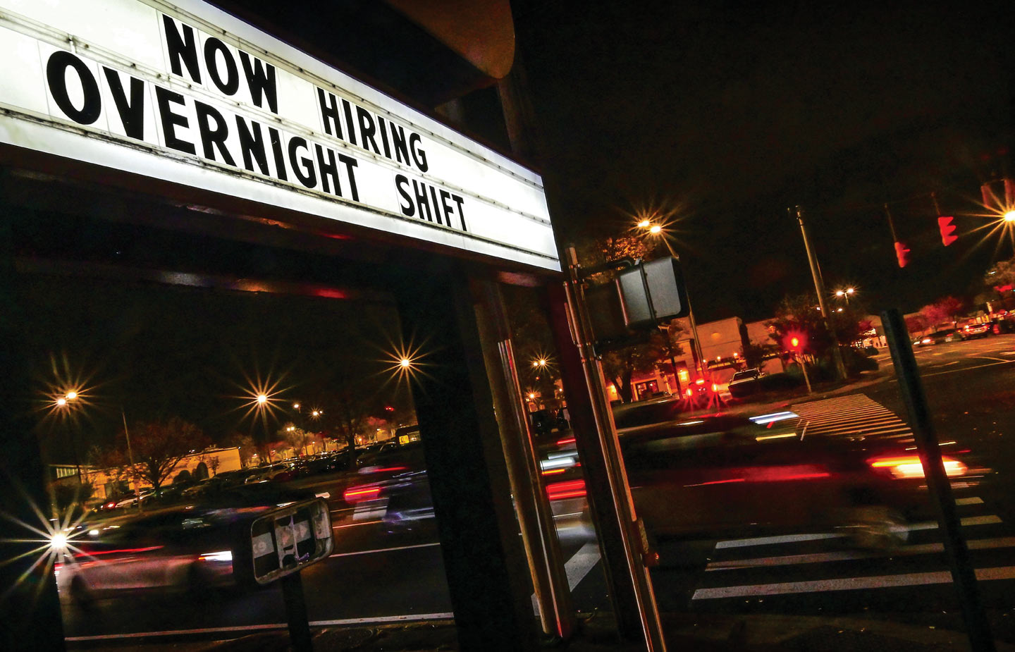 Image of "Now Hiring" sign in business parking lot at night