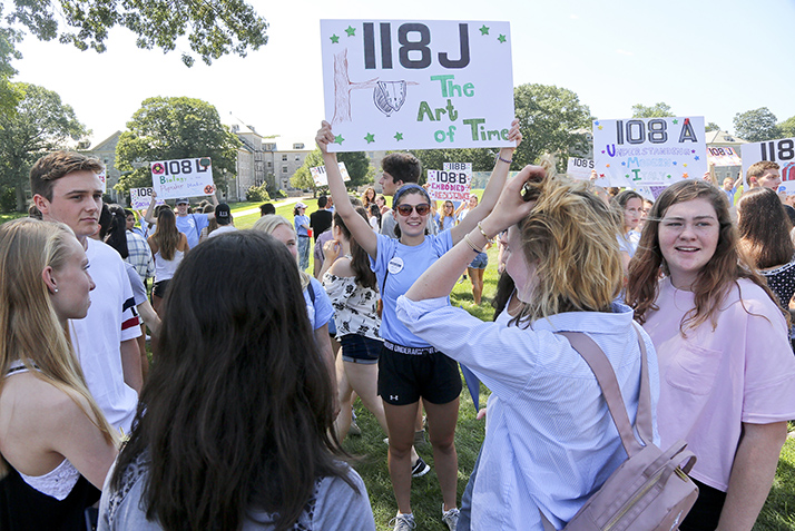 An student adviser holds a sign with the name of a first year seminar.