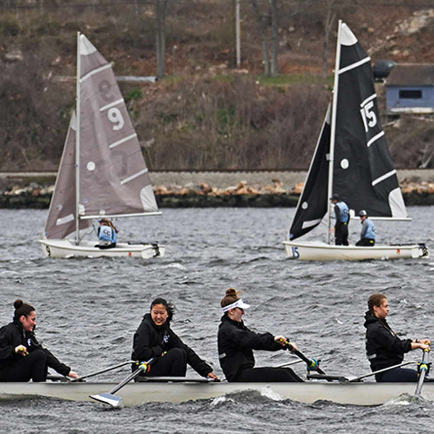 Image of crew members rowing in front of the sailboats