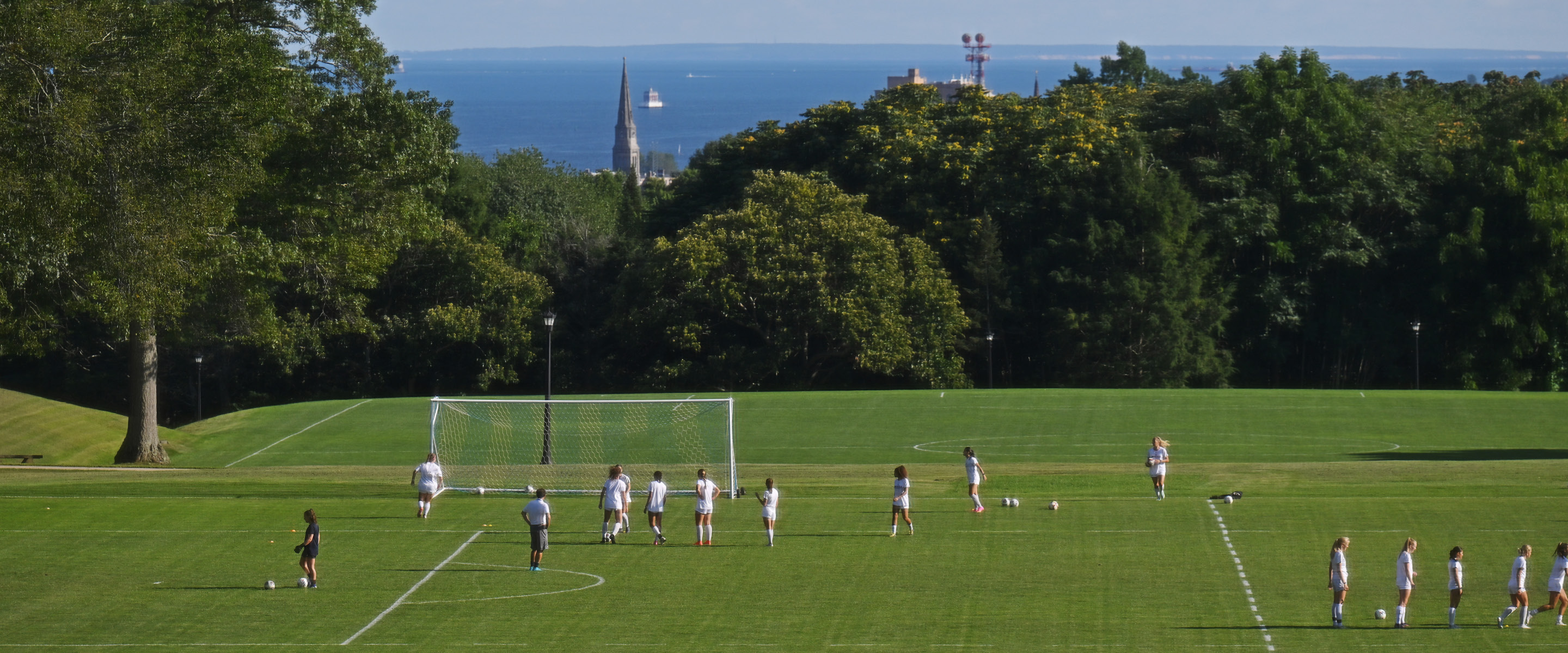 Panoramic shot of the Green with soccer practice on the field and Long Island Sound in the background.