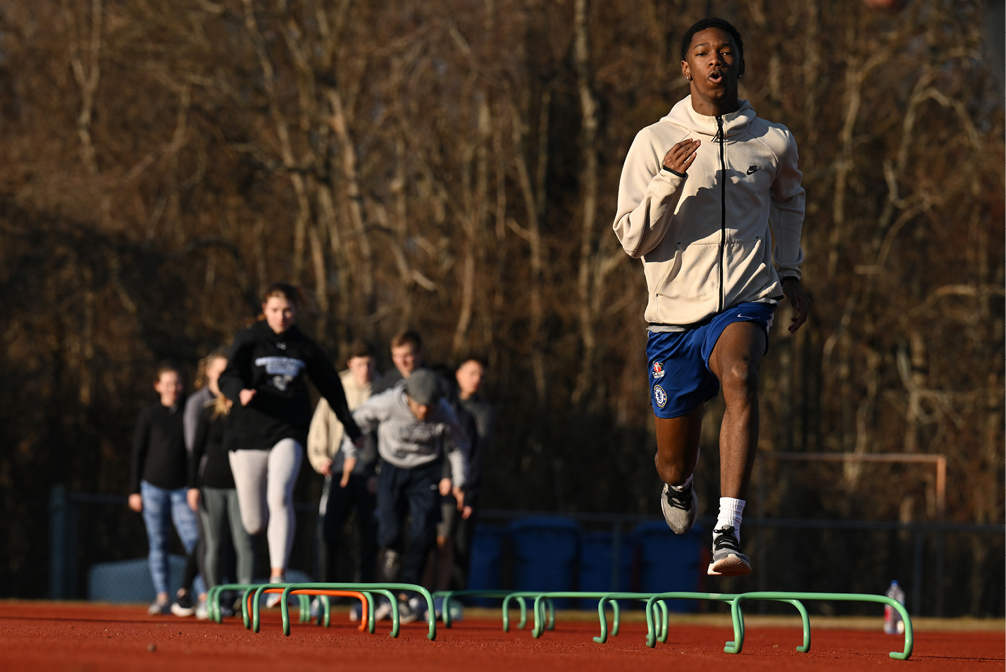 Jayson Firmin ’26 jumping over hurdle simulators at track & field team practice.