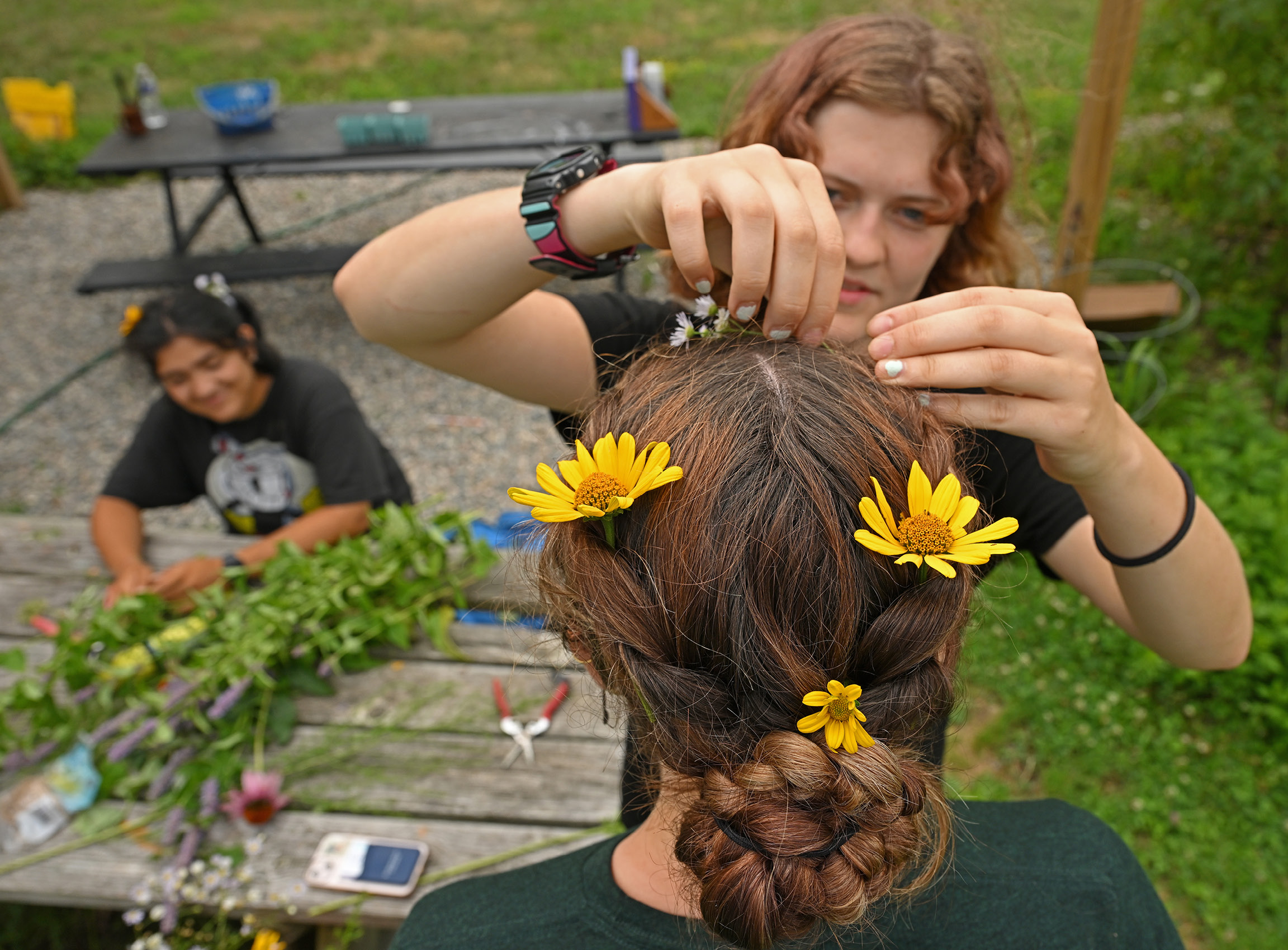 A Sprout worker ties flowers in another worker's hair