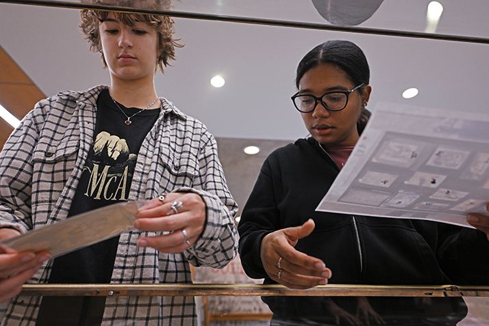 Leah Lorenz ’27, left, and Adismel Santana ’25 begin to arrange photographs in a display case in Shain Library.