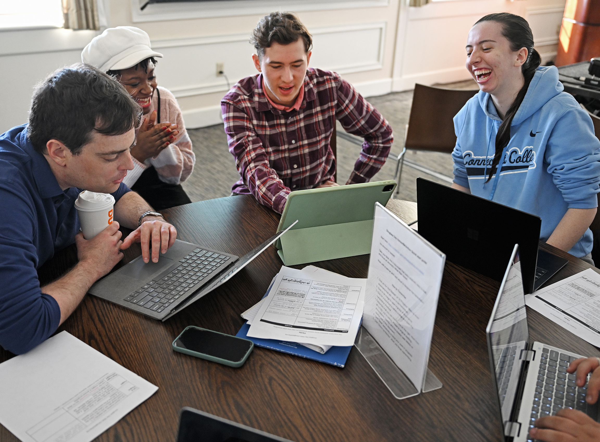 students and professor gather around laptop computer