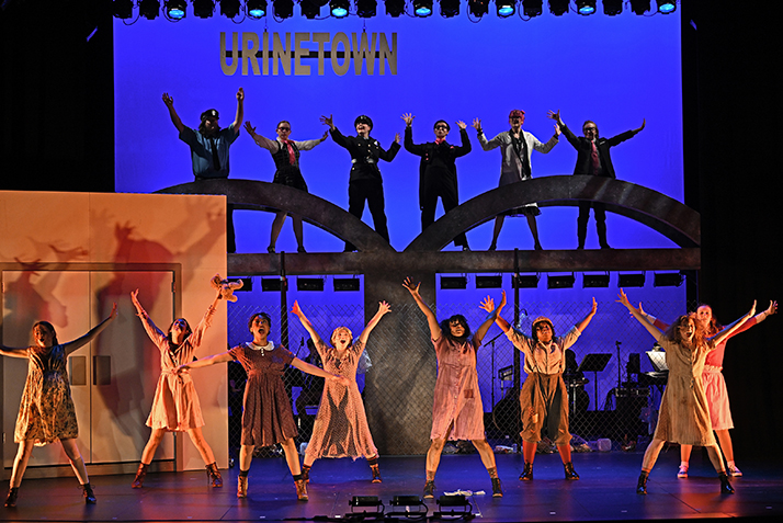 two rows of actors on two levels of the stage with arms raised