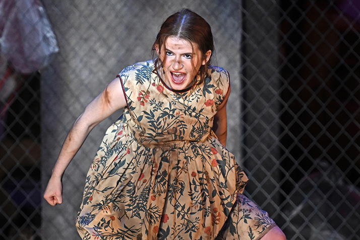 Actress in ratty flowered dress sings with angry facial expression