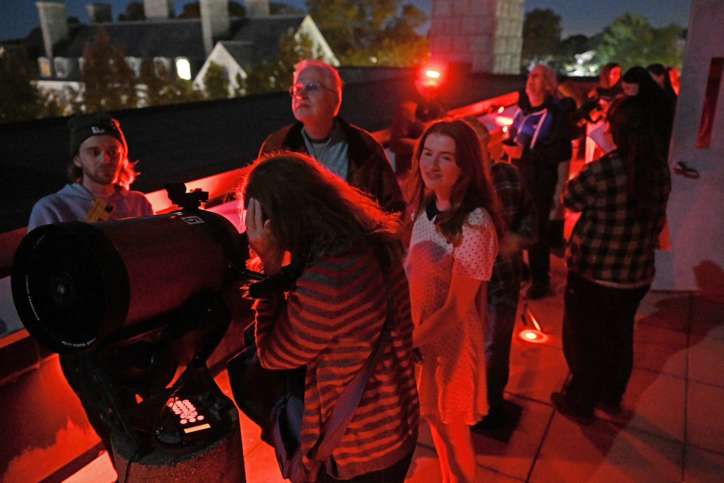 People gather to look at the skies through telescopes under the red light of an observatory open house.