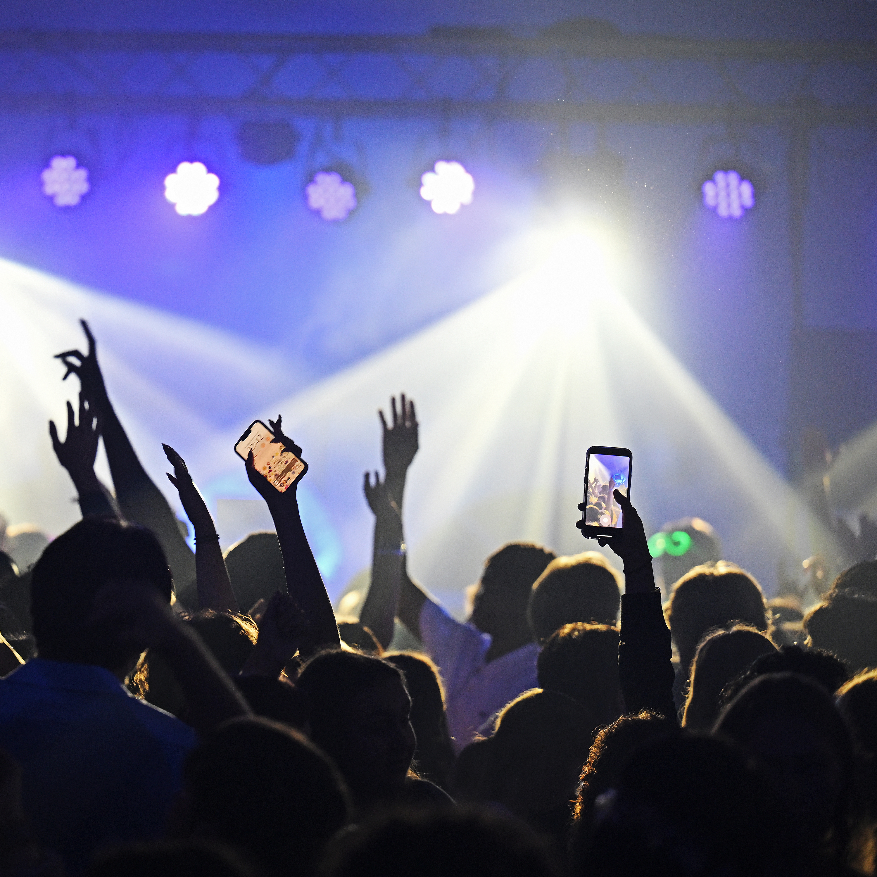 students, arms raised, dance in the flashing lights from a DJ on stage