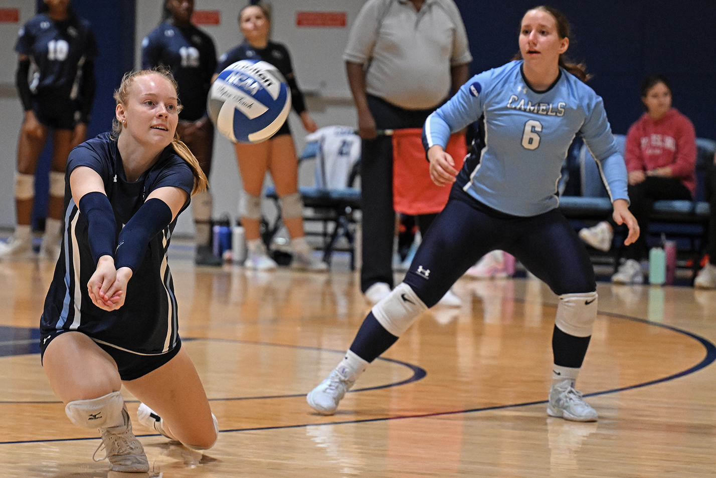 A volleyball player lunges for a dig as another watches