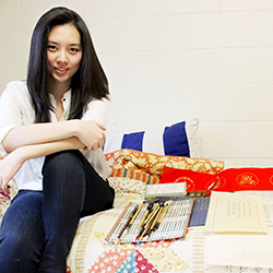 Lu Shan Zhang '14 poses with some of her calligraphy work and the supplies she brings with her to campus from China. Photo by Miguel Salcedo '14.